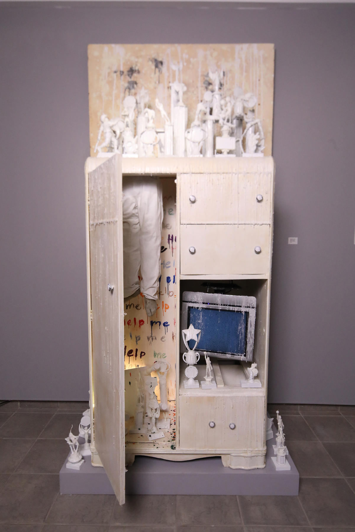 A found object sculpture featuring a dresser, small white sculptures and other objects.