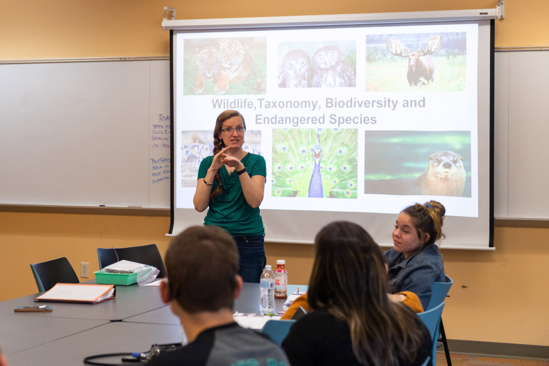 woman standing in front of a projector screen in a classroom using sign language.