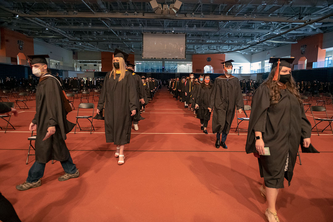 Students wearing graduation regalia processing up an aisle in two lines.