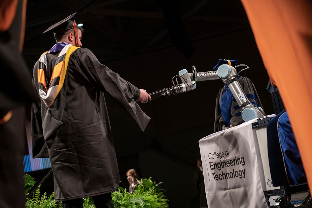 robotic arm handing diploma to graduate.