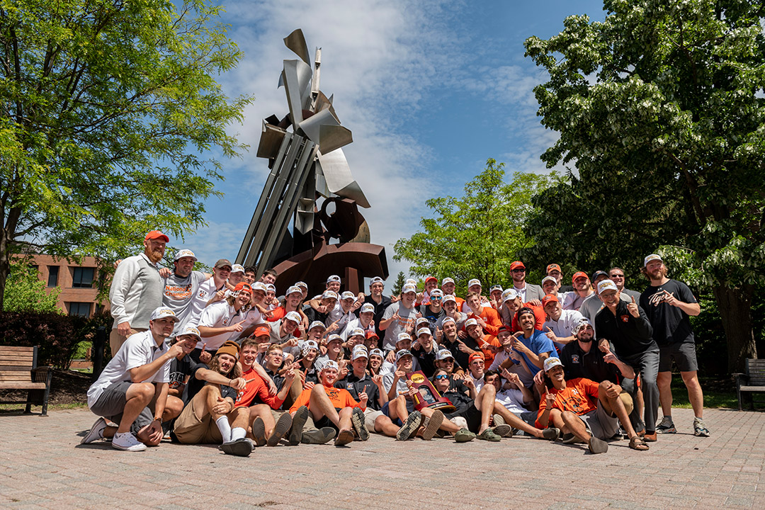 men's lacrosse team gathers in front of the Sentinel statue.