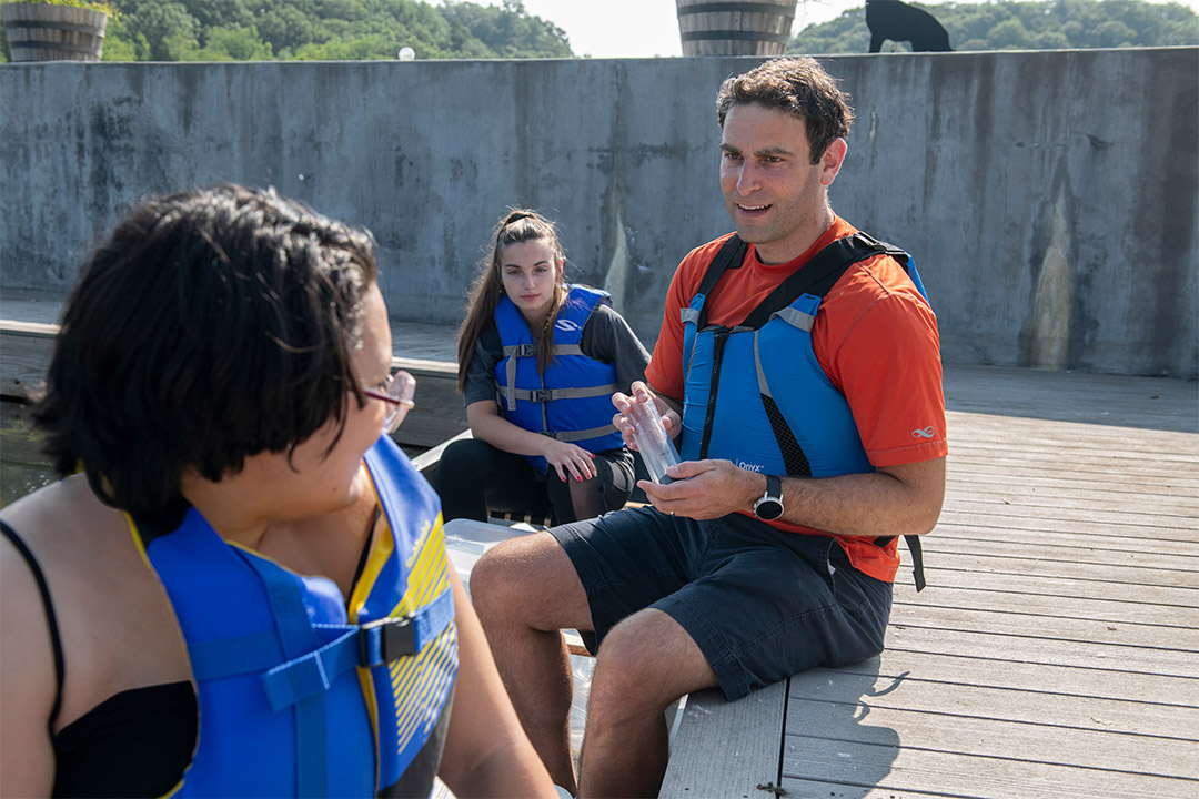 three researchers wearing life vests sitting on a dock.