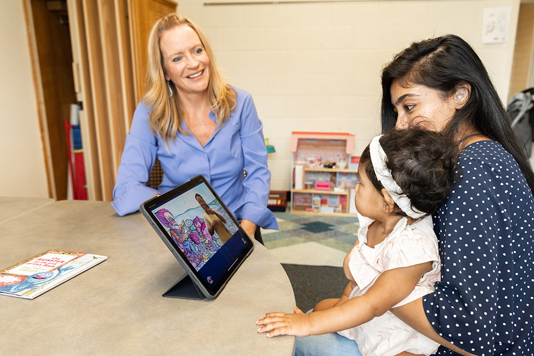 researcher observing a child and mother looking at a tablet.