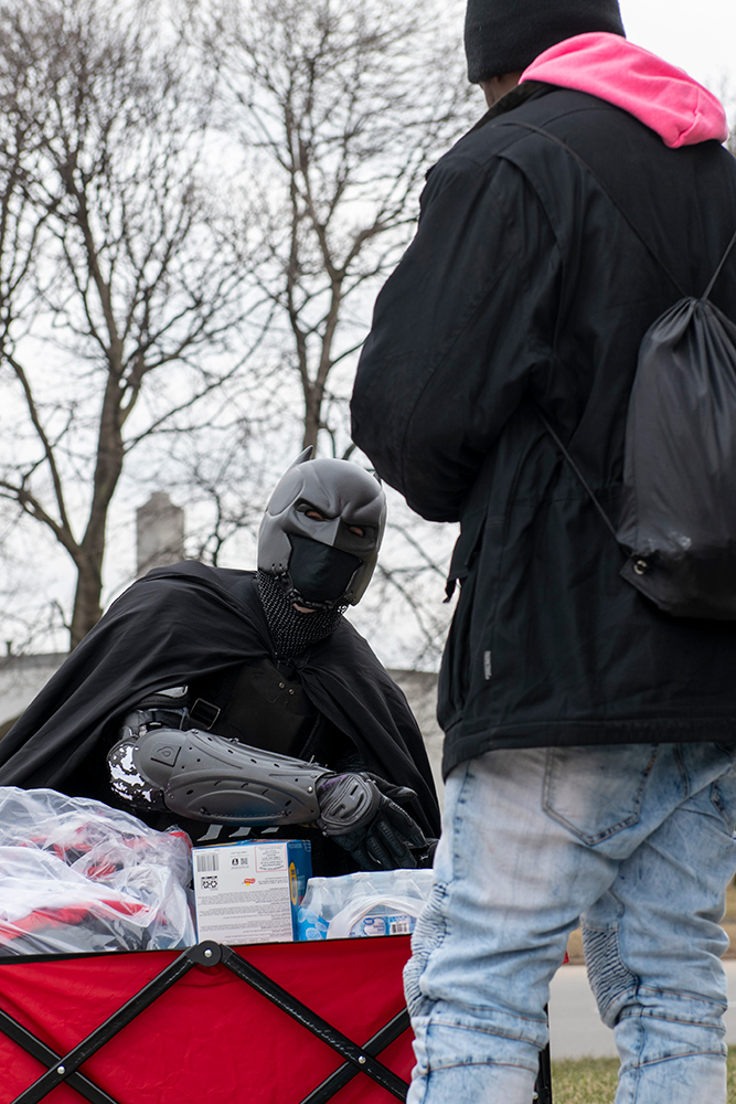 person dressed as Batman talking to a homeless person.