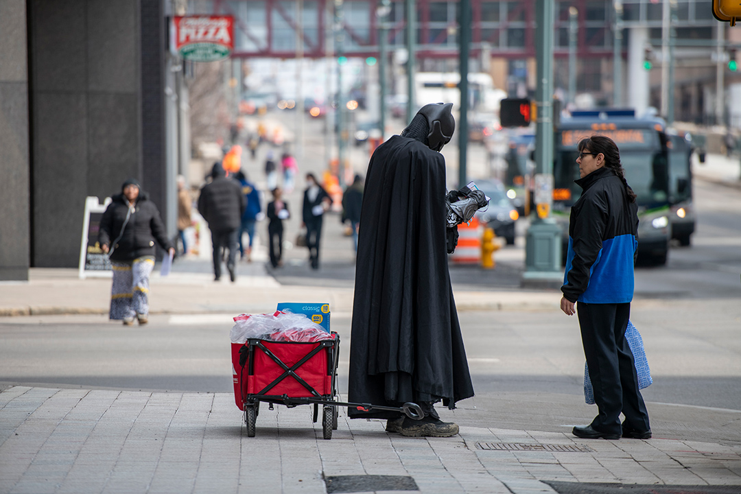 person dressed as Batman talking to a woman on a sidewalk.