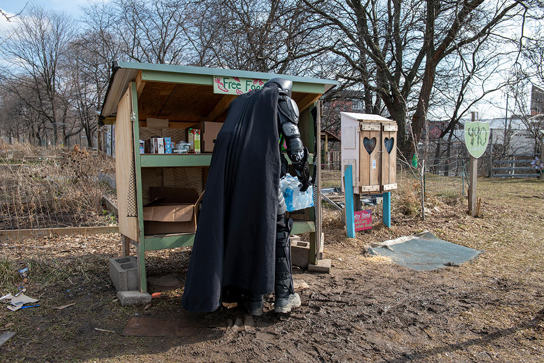 a person dressed as Batman putting food into an outdoor pantry.