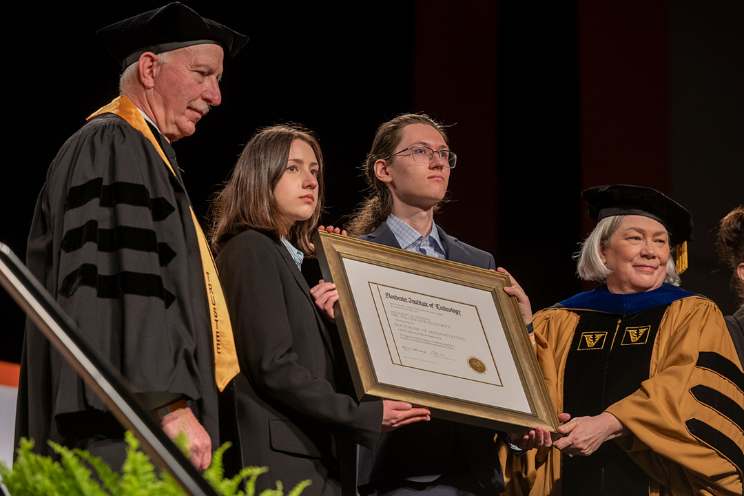 two students receiving plaque from college administrators.