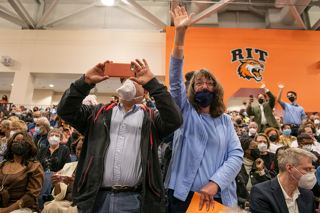 two people in the audience standing up to wave and take a photo.