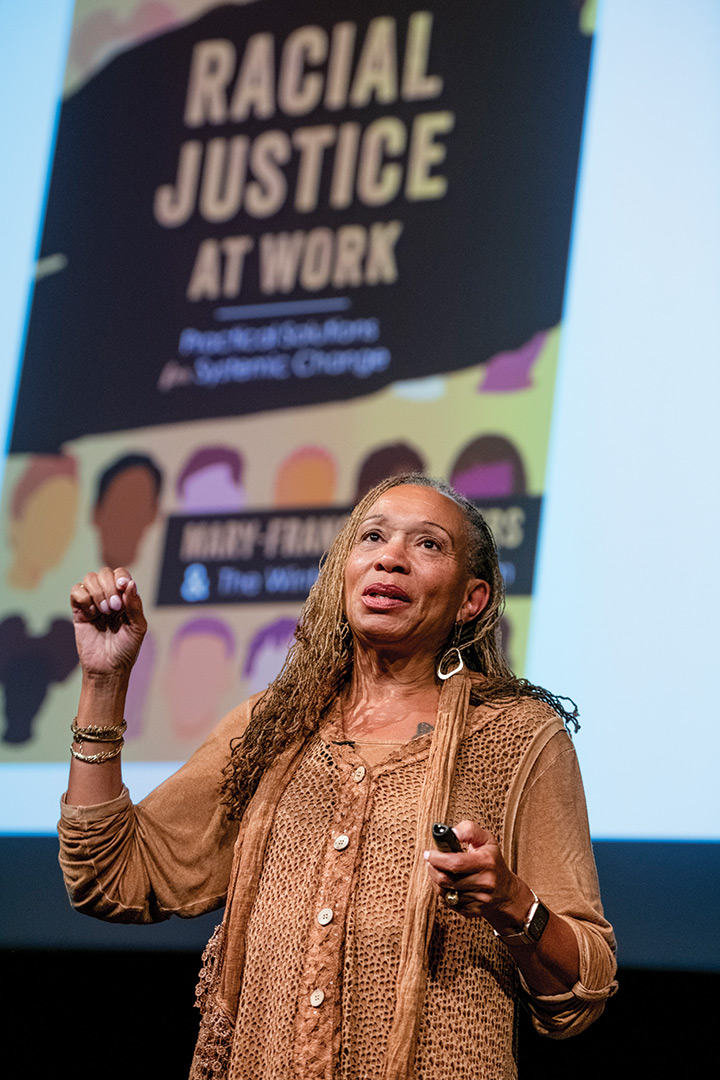 woman speaking in front of a poster that reads, racial justice at work.