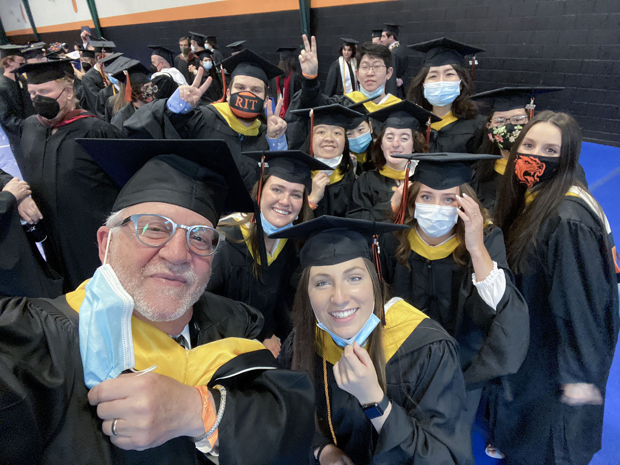 Ten students pose for a photo with Michael Peres at gradation in caps and gowns.