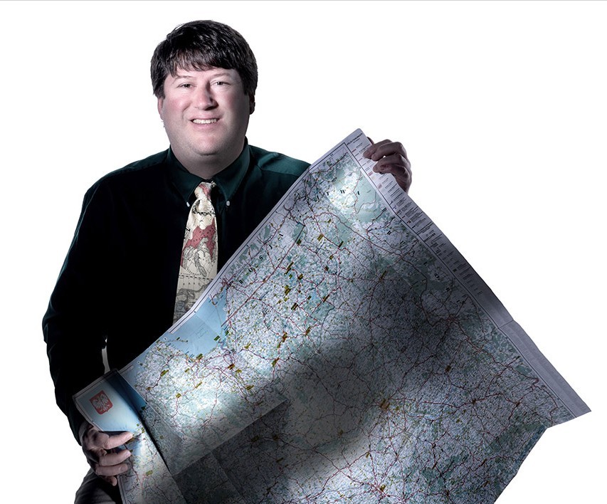 Man in black shirt and tie holds map of Poland.