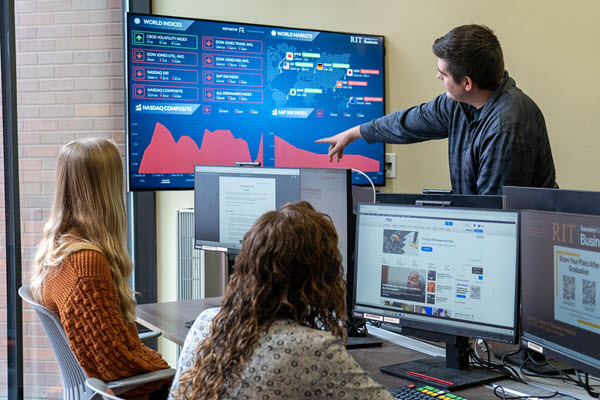 Three students analyzing real-time financial market data in business lab