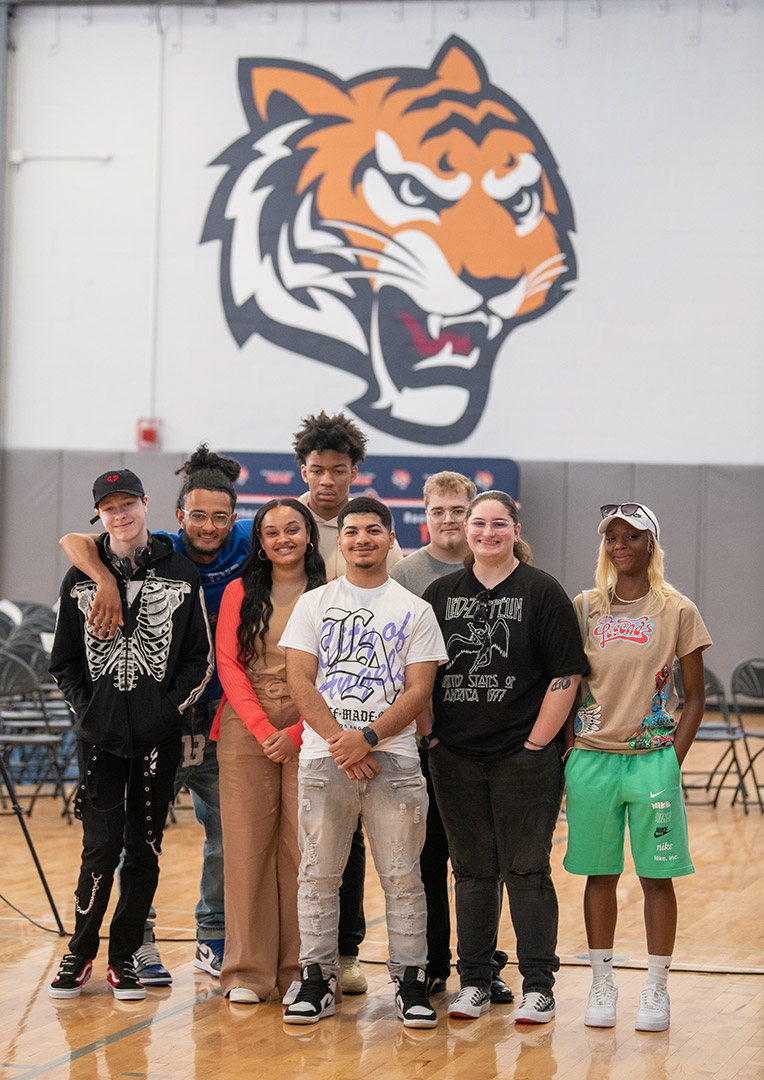 eight high school students posing for photo in a gym with a tiger logo on the wall.