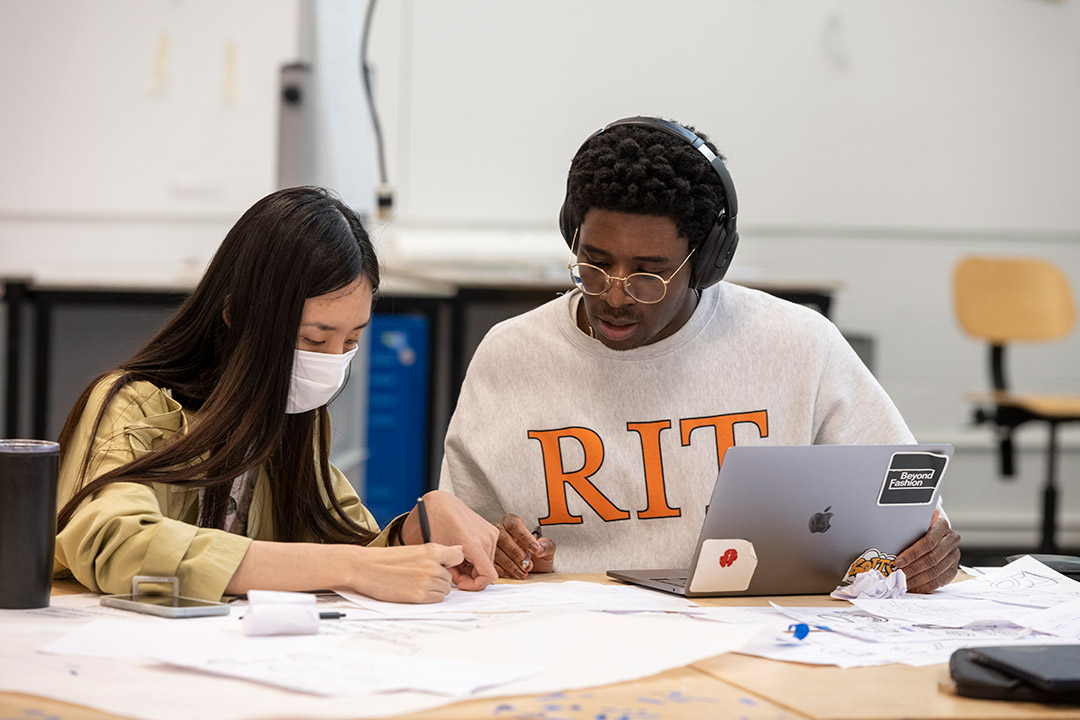 two college students drawing on a large piece of paper.