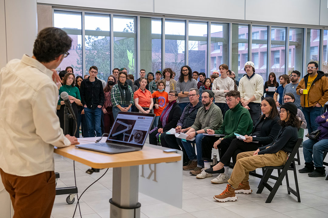 classroom of college students standing and sitting while listening to a presentation.