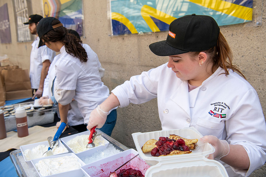 college student wearing a chef coat scooping food into a take out container.