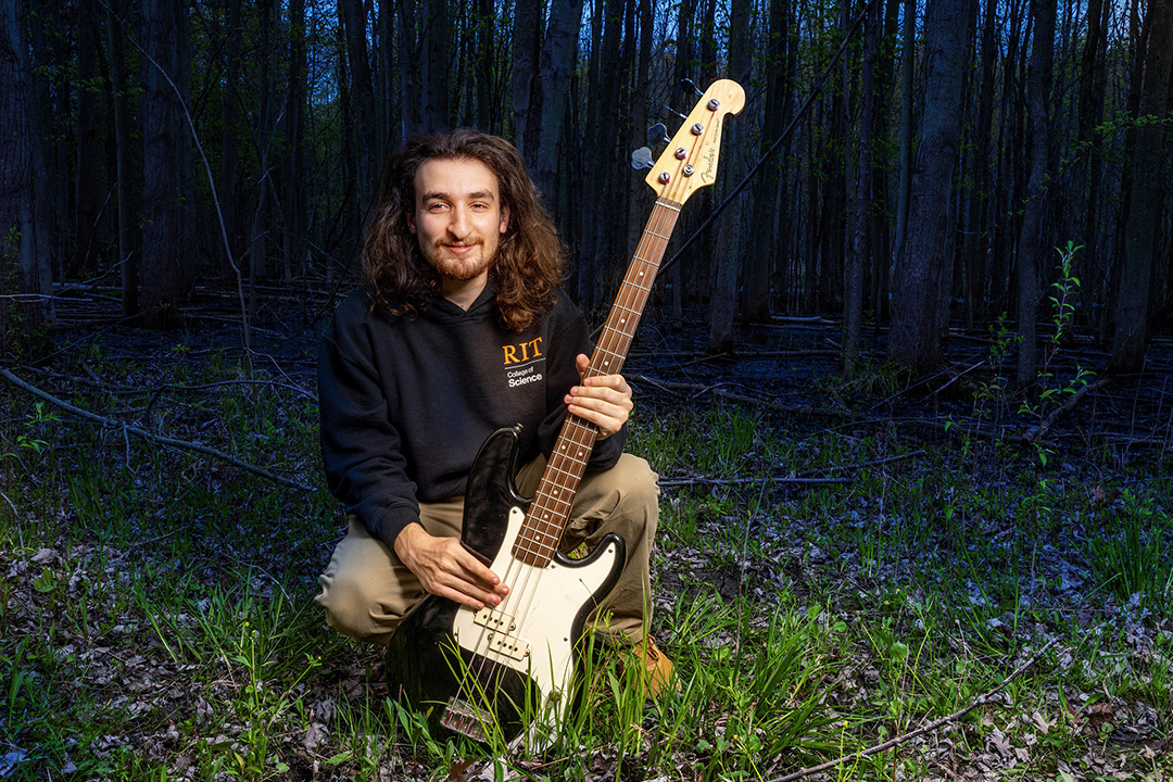 college student crouched down holding up a guitar.