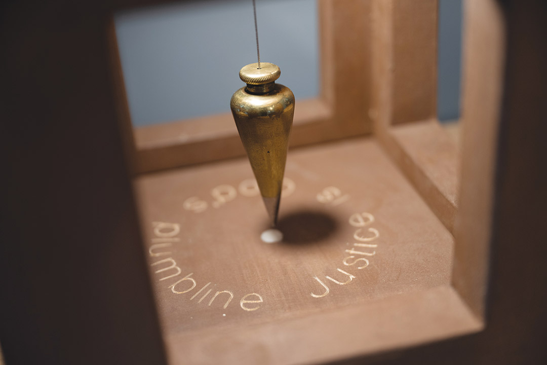 closeup of a wood art piece with a cone shaped piece suspended by a wire.