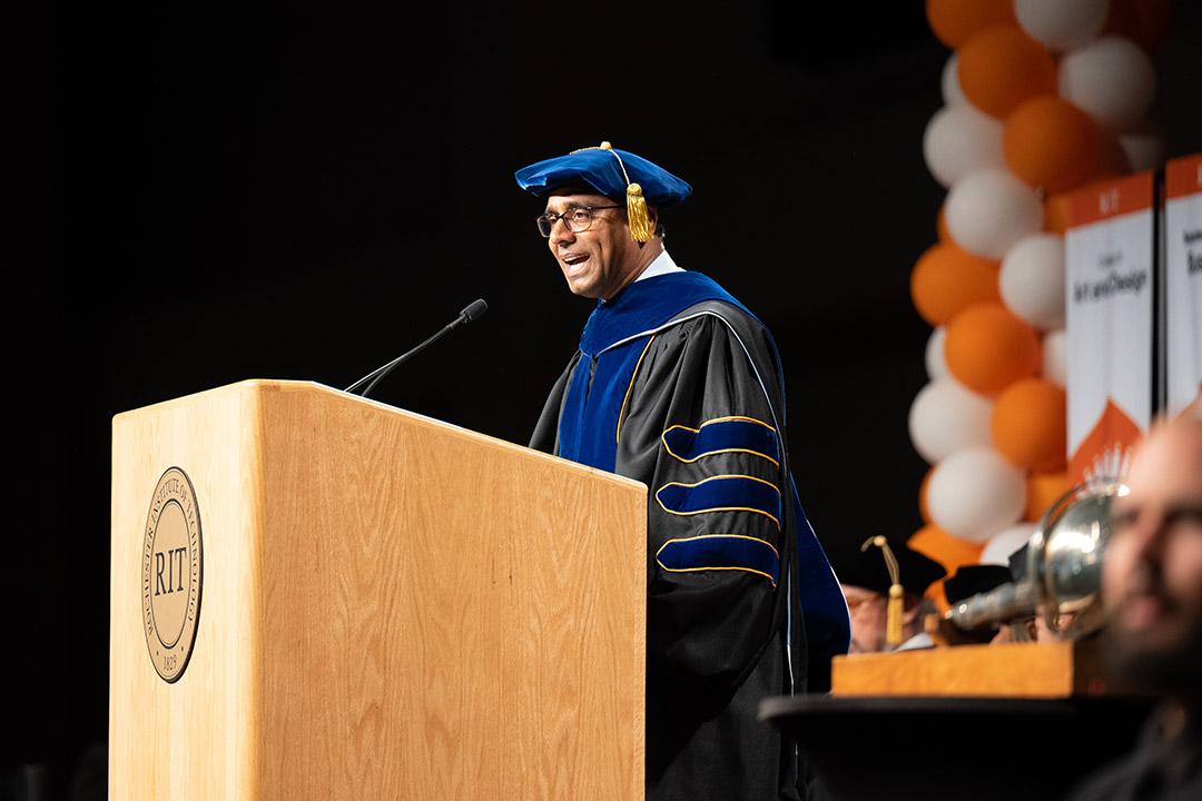 person wearing academic regalia speaking at a podium.