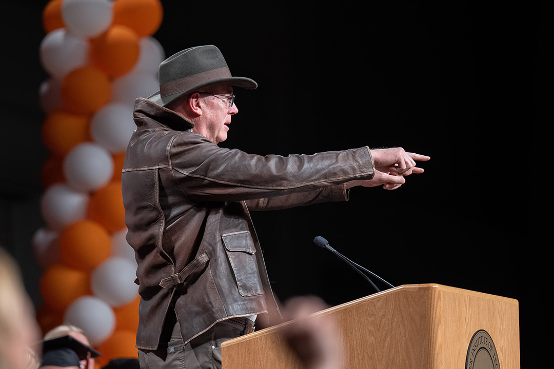 R I T president wearing an Indiana Jones outfit and pointing to the students from a podium.