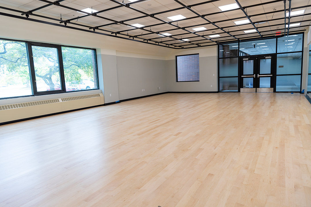 a dance studio room with a wooden floor and lighting grid on the ceiling.