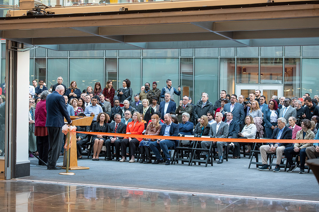 man speaking at a podium facing a crowd of seated people.