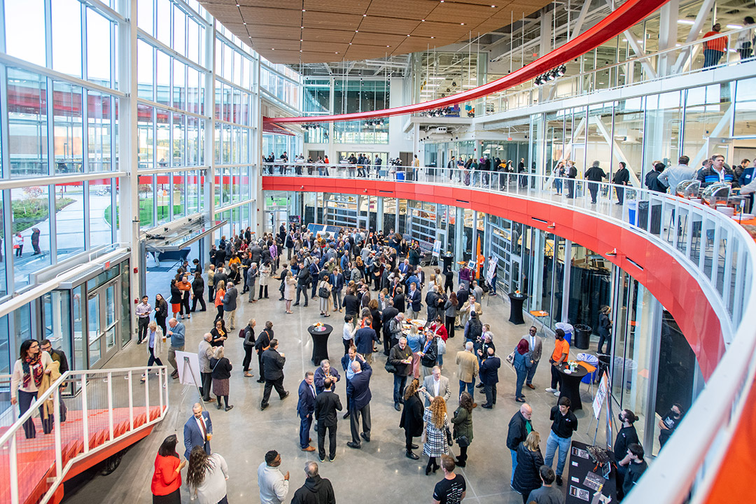 crowd of people gathered in the atrium of a rounded building with glass walls.