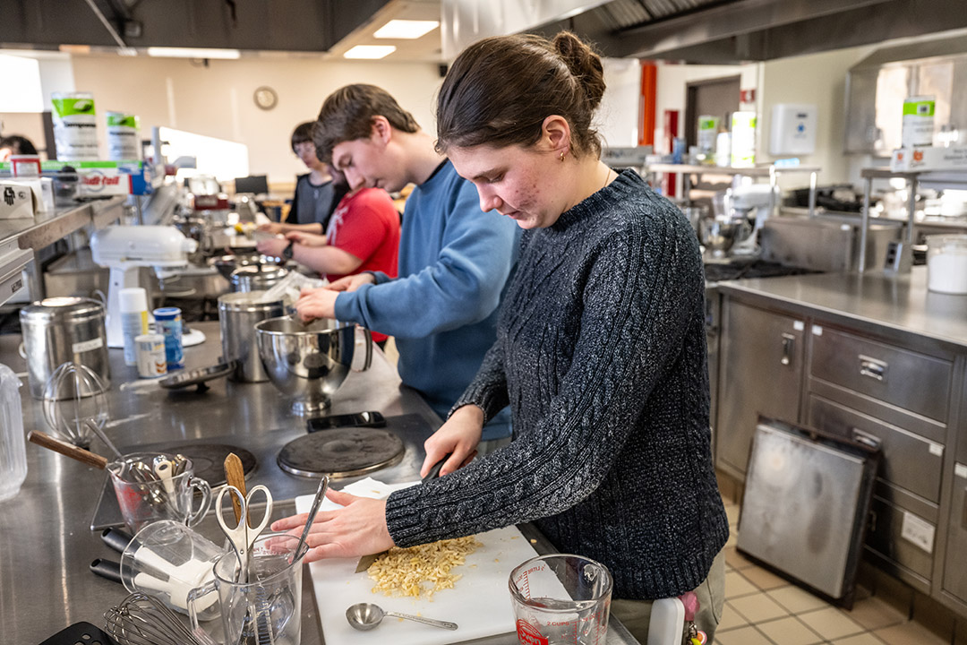 college students working in a large kitchen, chopping nuts and stirring contents of a mixing bowl.
