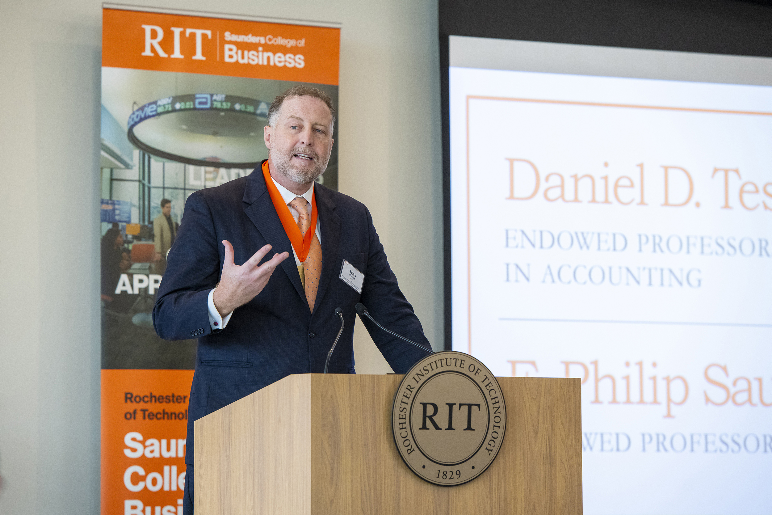 A man in a suit speaks at a podium