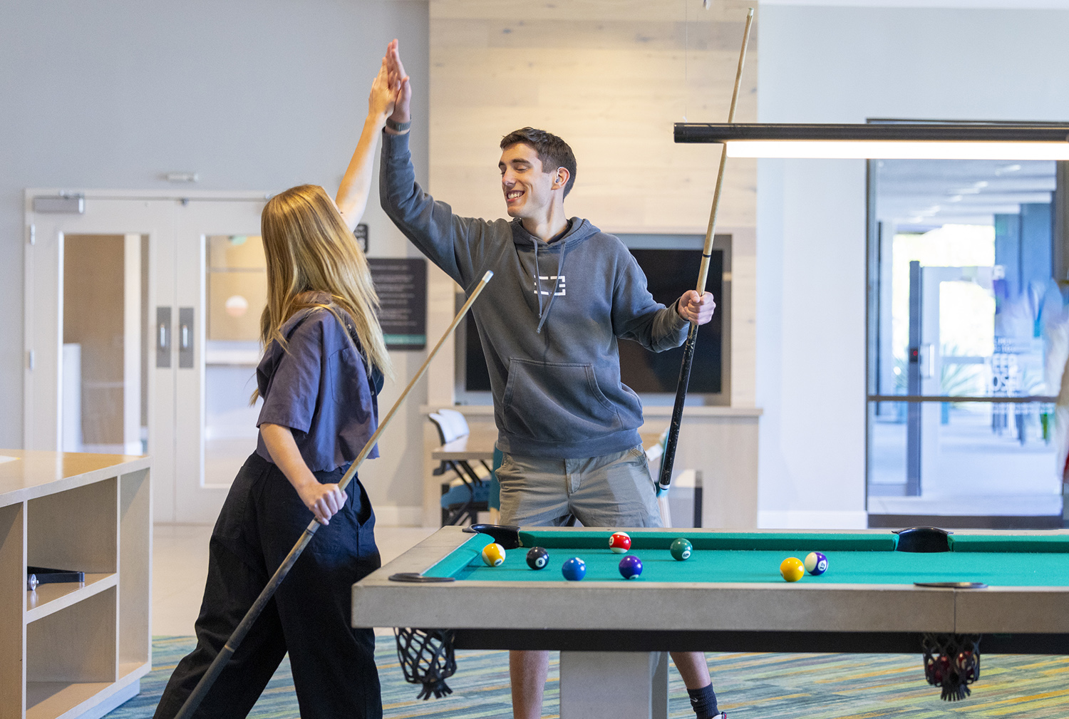 Two students high-five while playing billiards.