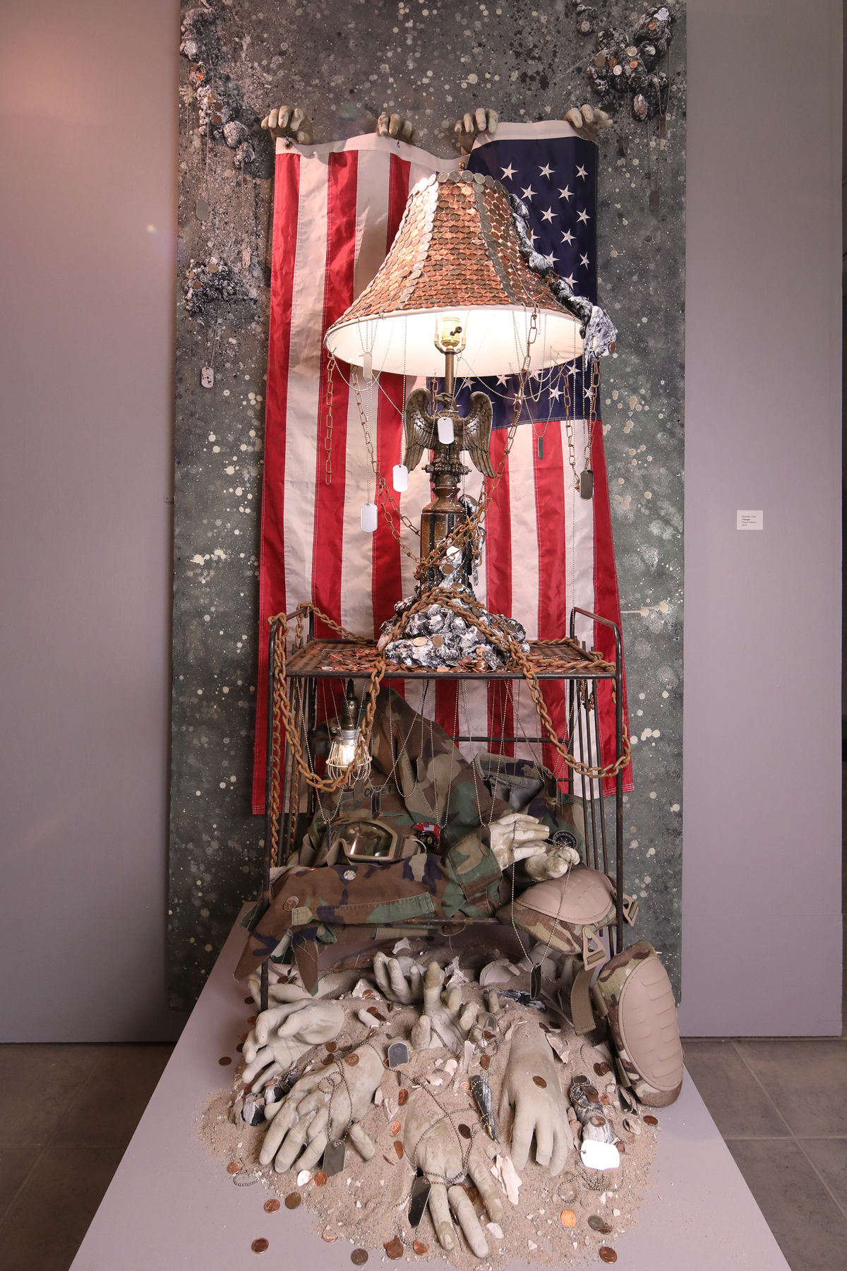 A found object sculpture featuring an American flag, a lamp with an eagle sculpture and chains.