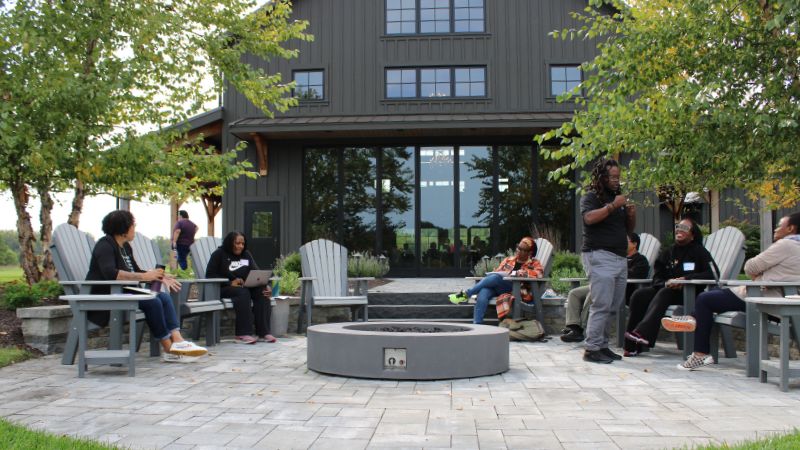 a photo of participants outdoors at the tait preserve conversing in the fire pit area by the water