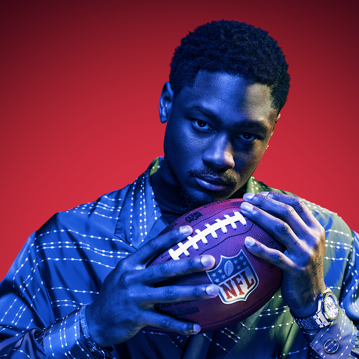 Stefon Diggs holding a football against a red background.