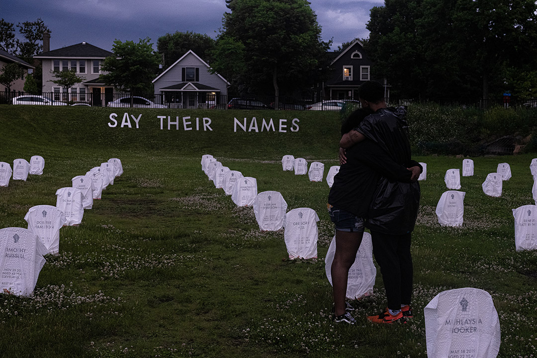 a cemetery with small, rounded tombstones and a sign that says: Say Their Names.