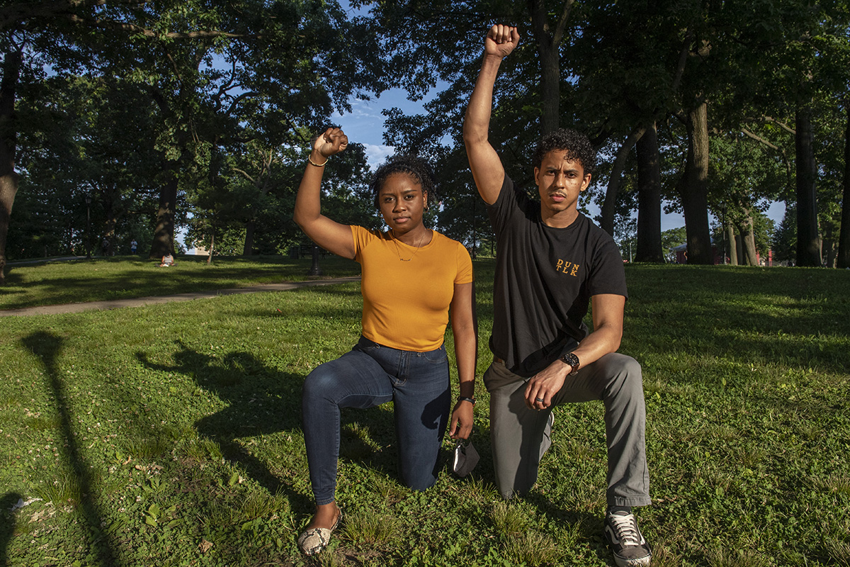 A girl and a boy pose, on a knee with their right arms raised. 