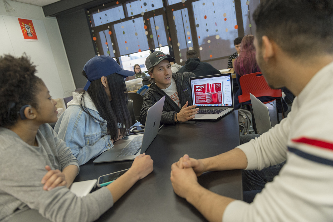 Studens sitting at a table show off their designs