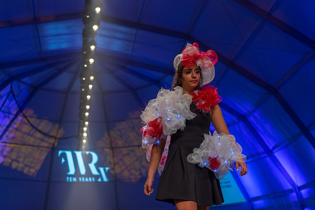 Student walks runway wearing red and white mesh piece.