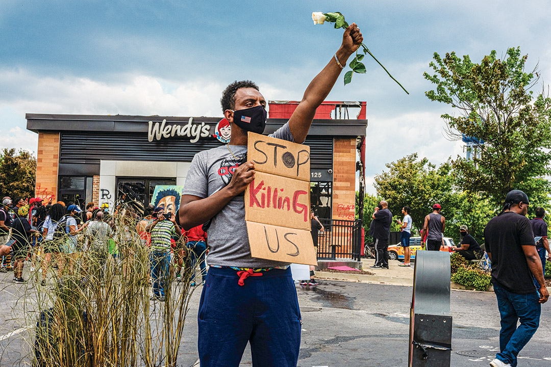 a man standing in front of a Wendy's restaurant holding a rose and a sign that reads: Stop Killing Us.