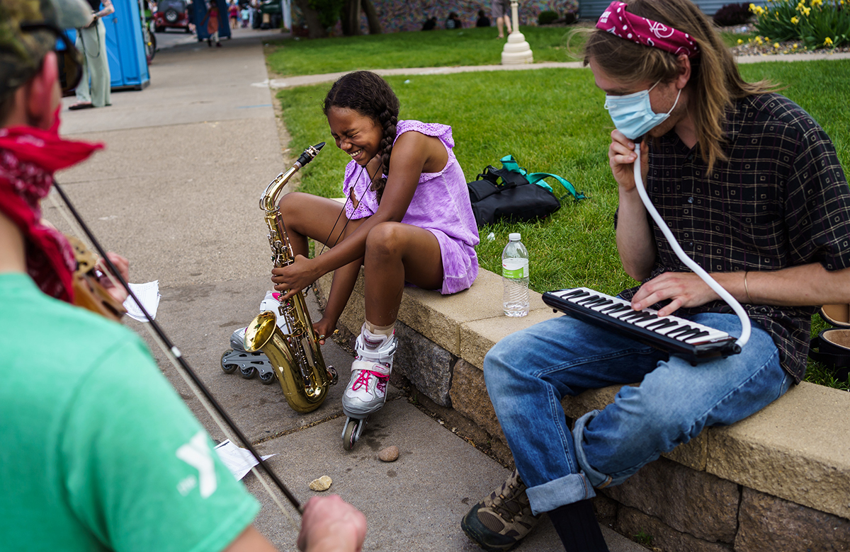 A girl plays the saxophone while sitting next to a man.