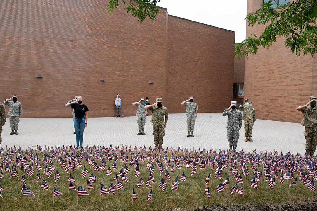 ROTC cadets saluting in front of a field of small American flags.