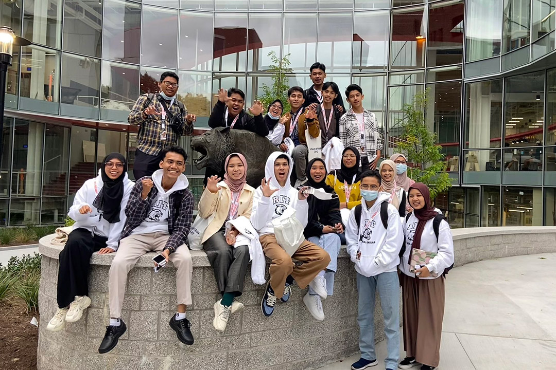 college students from Indonesia sitting and standing around a tiger statue outdoors.