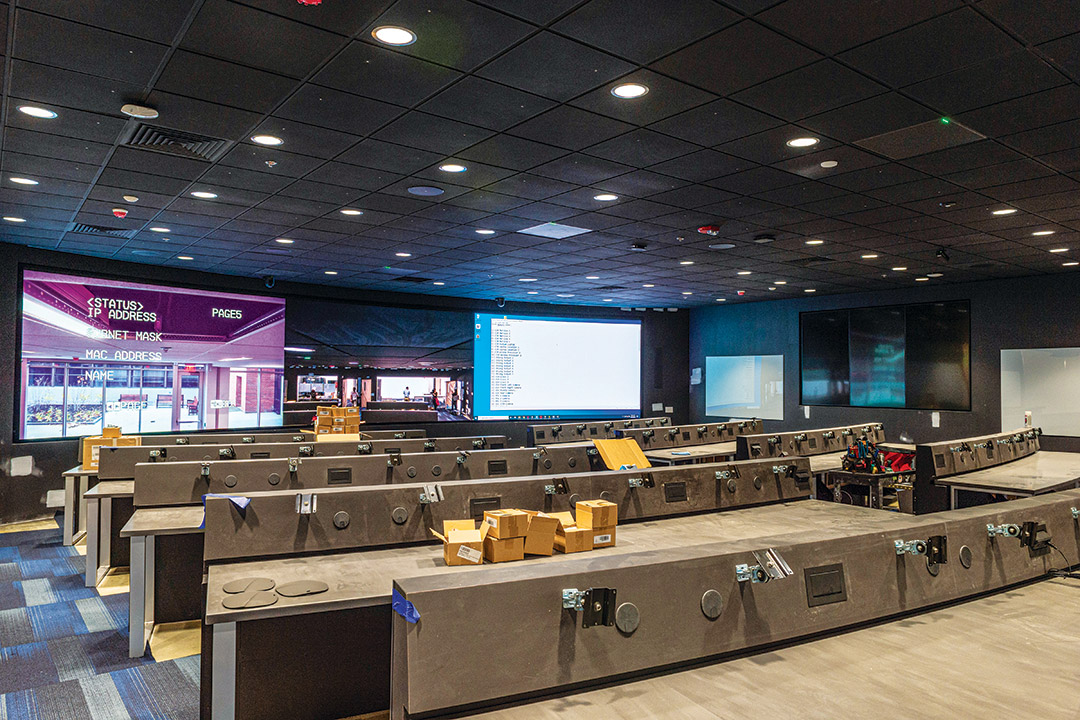 large room with long desks and large TV screens.