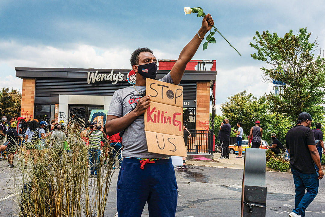 man holding a white rose and a sign that reads "stop killing us."