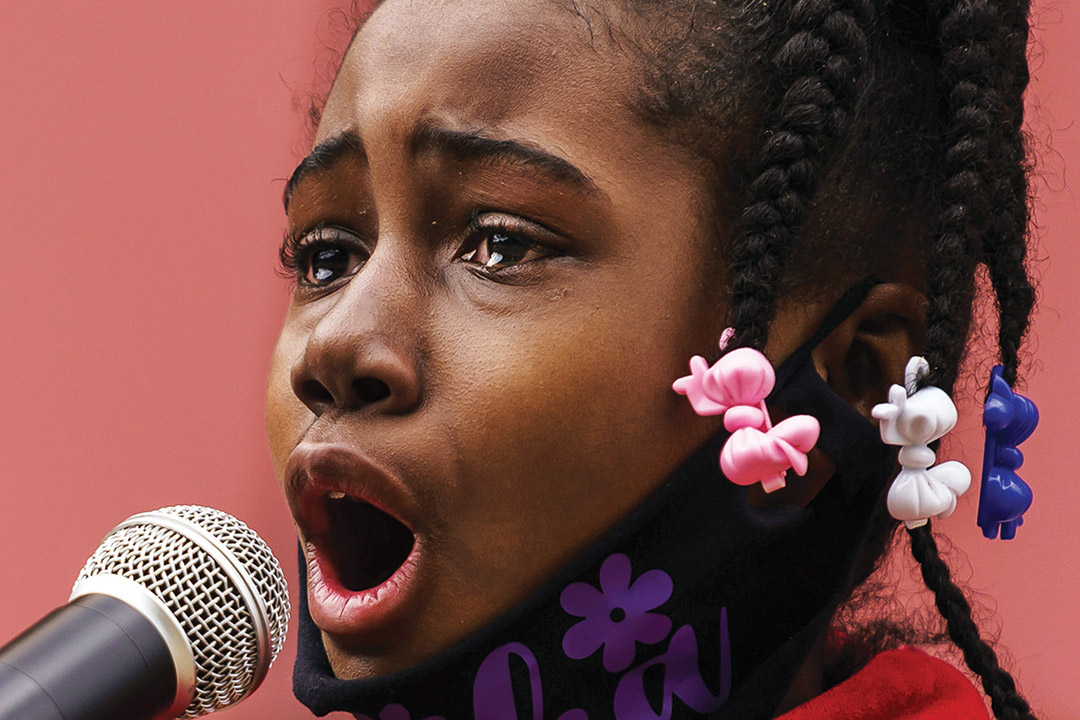 close-up of Black girl speaking into a microphone with tears in her eyes.