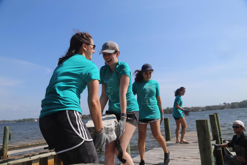 Students carry large rocks down a pier.