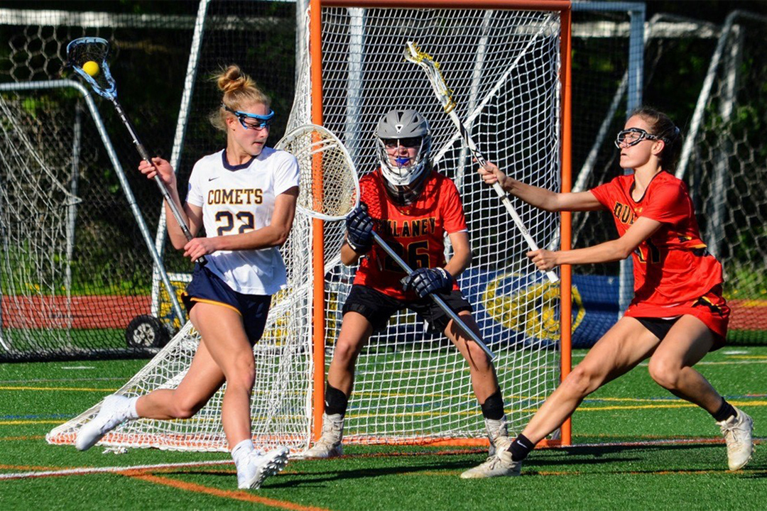offensive player, defensive player and goalie playing in a high school women's lacrosse game.
