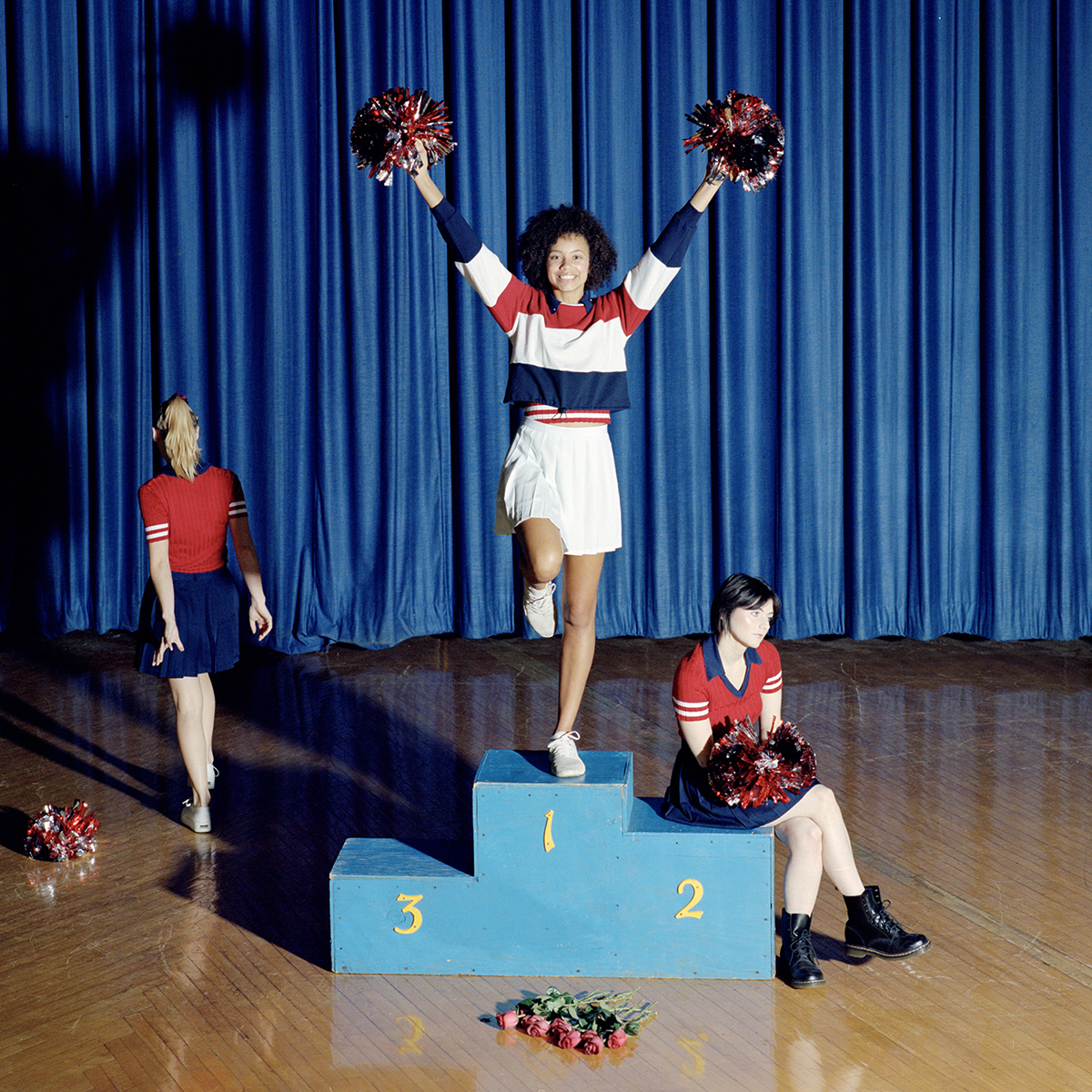 Portrait photography of a cheerleader standing on a podium while another cheerleader walks away and one sits on a podium.