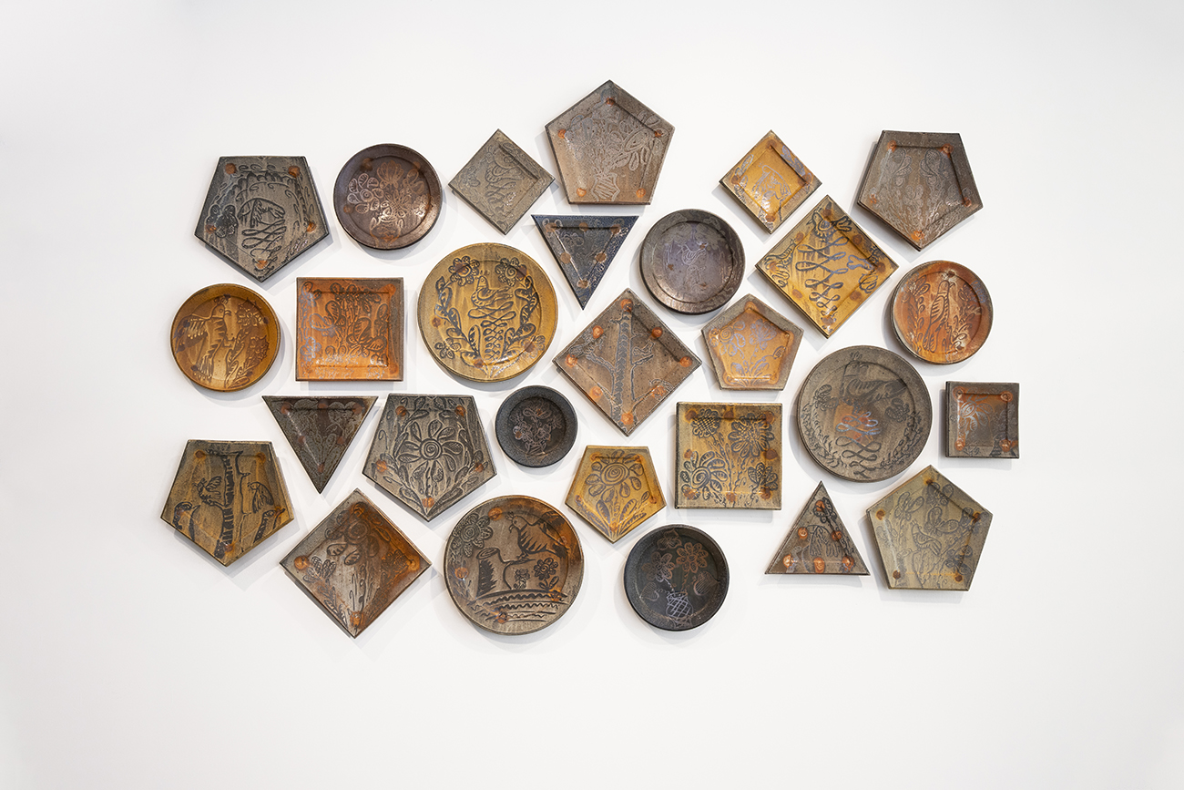 An assortment of more than a dozen ceramic platters on a gallery wall, representing functional pottery examples.