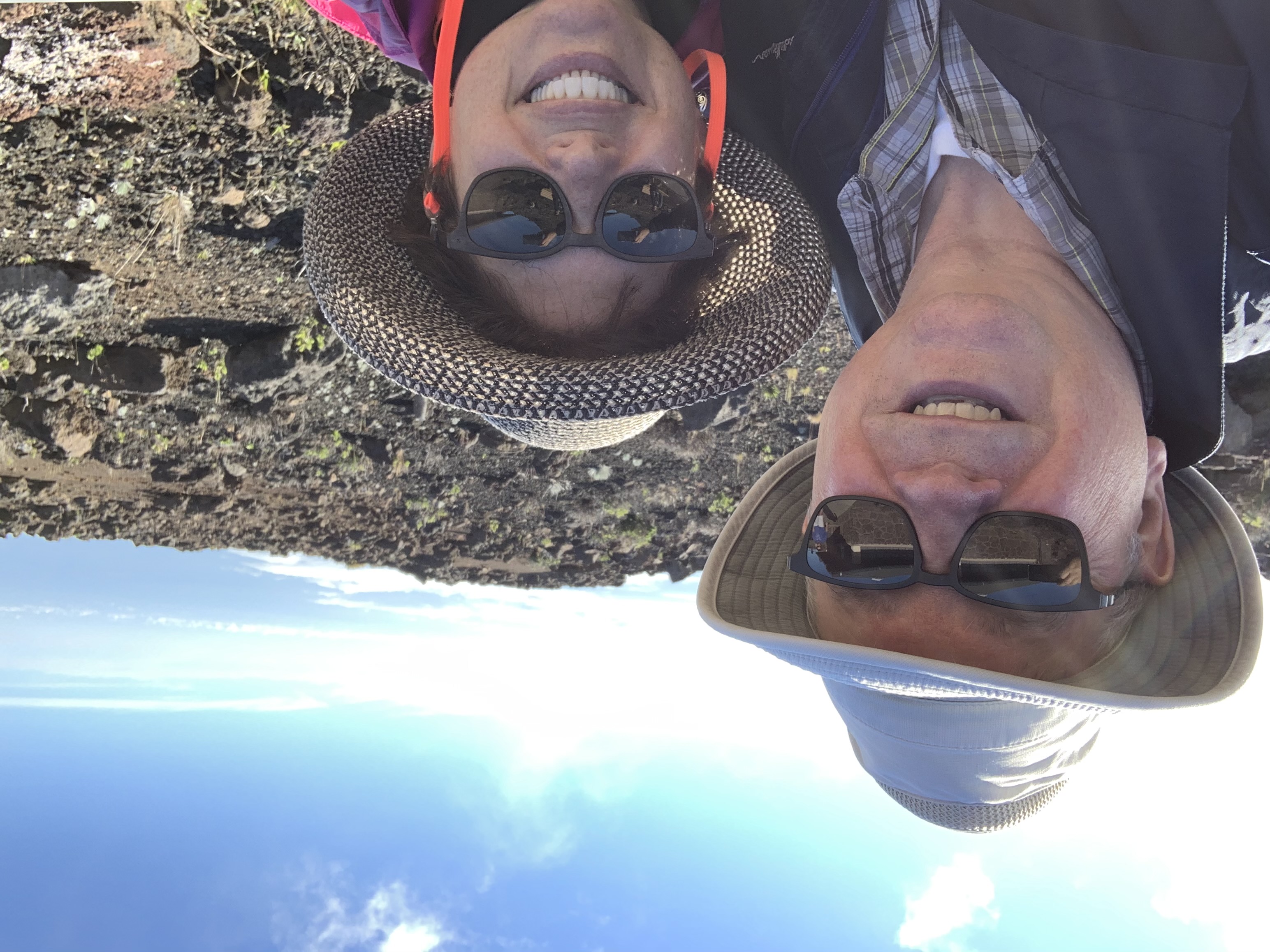 A selfie of two people with hats, hiking.