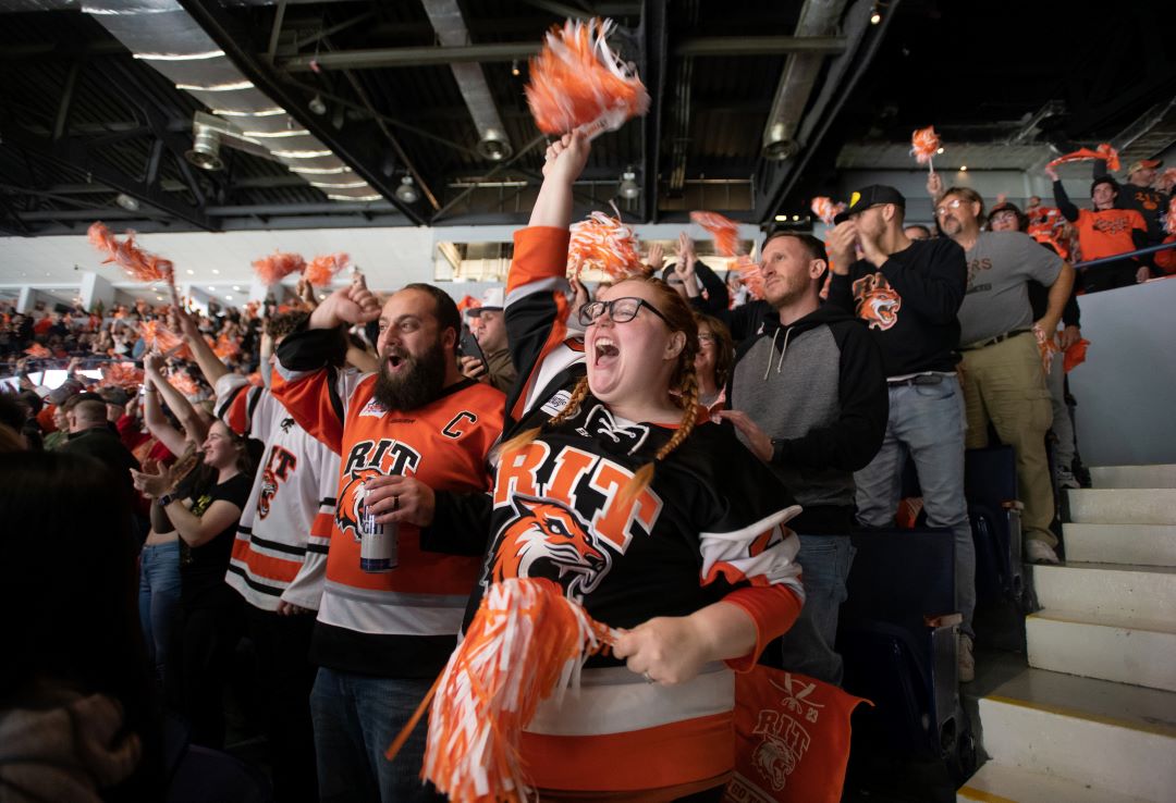 Students in RIT hockey jerseys cheer and wave pom poms.